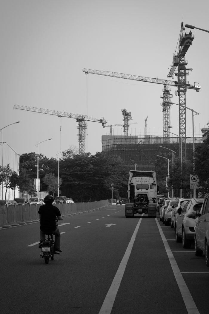 Black and white urban street view with cranes, scooter, and construction site.